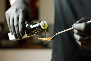 Person with black gloves pouring seed oil on spoon for smoothie preparation photo