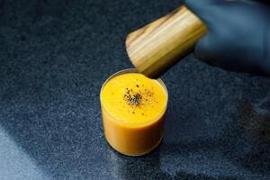 Mango Carrot Apple Smoothie in a glass on dark background with glass straw photo