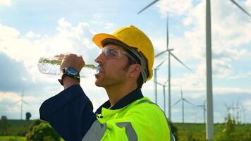 Smart engineer wearing protective helmet drinking water while working at electrical turbines field video