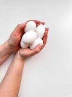 manos de plataforma un racimo de blanco huevos en contra pálido fondo, un símbolo de cuidado, alimento, y nuevo principios con amplio Copiar espacio. para culinario sitios web, receta blogs, y nutricional guías foto