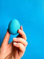 mano equilibrio azul huevo en un punta del dedo en contra sólido azul fondo, minimalista concepto para balance, Pascua de Resurrección, y sencillez con espacio para texto. foto