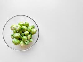 Brussels sprouts in transparent glass bowl on white background with ample space for text, healthy food concept. photo