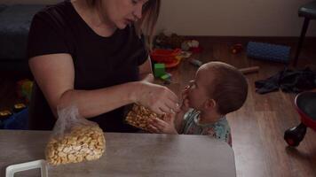 mam zit met een kind en geeft koekjes tegen de achtergrond van verspreide speelgoed video