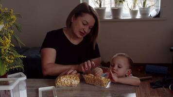 Mama mit ein Kind nehmen Kekse aus von ein Tasche auf das Tisch. video