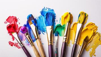 An arrangement of colorful paintbrushes dipped in various hues of paint on a pristine white surface photo