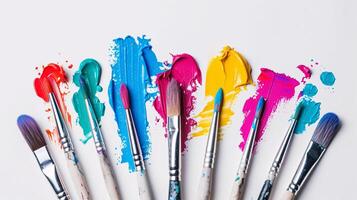 An arrangement of colorful paintbrushes dipped in various hues of paint on a pristine white surface photo