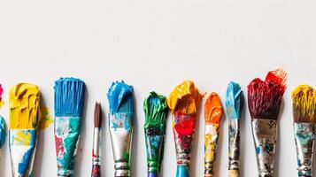 An arrangement of colorful paintbrushes dipped in various hues of paint on a pristine white surface photo