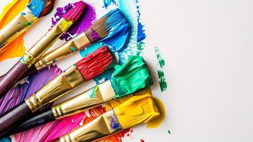 An arrangement of colorful paintbrushes dipped in various hues of paint on a pristine white surface photo