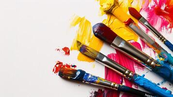 An arrangement of colorful paintbrushes dipped in various hues of paint on a pristine white surface photo