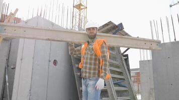 construtor homem dentro capacete de segurança e colete carregando madeira em construção local dentro dele trabalhando dia video