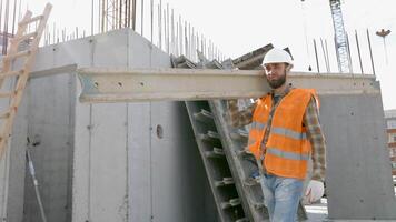 constructor hombre en casco de seguridad y chaleco que lleva madera en edificio sitio en su trabajando día video