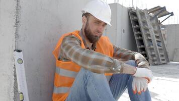 constructor reparador, capataz en la seguridad casco y chaleco sentado abajo a descanso a lugar de trabajo en edificio siguiente a herramienta caja y regla video