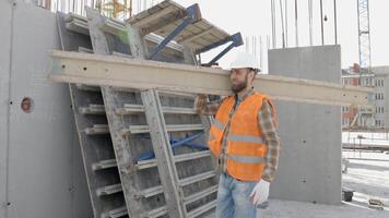 byggare man i Hardhat och väst bärande timmer på byggnad webbplats i hans arbetssätt dag video