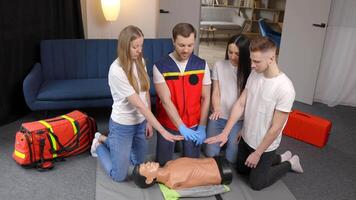 Young man instructor helping to make first aid heart compressions with dummy during the group training indoors video