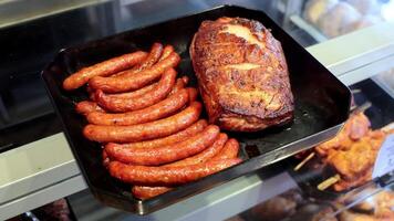 grelhado salsichas e assado carne de porco em bandeja, grelhado salsichas ao lado uma assado carne de porco articulação dentro uma Delicatessen exibição bandeja. video