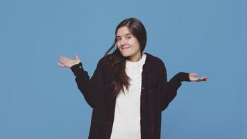 Young attractive woman spreads her hands with perplexed smile on her face on a blue background in the studio. Concept of accidental misunderstanding video