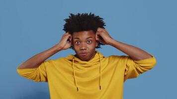 Portrait of a young black guy feeling extremely worried and shocked, touching her head and showing a mind explosion gesture on a blue background in the studio video