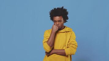 Young black guy thinking with a perplexed face stroking his chin with a hand on a blue background in a studio. Concept of searching for interesting and useful activities video