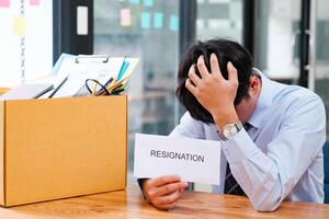 Man at desk with resignation letter, pondering his decision beside a packed box. photo