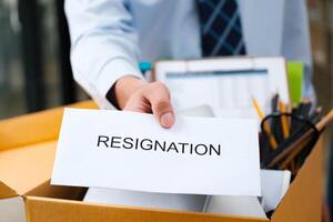 Man's hand presenting a resignation letter, office box with belongings in the back. photo