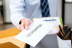 Man's hand presenting a resignation letter, office box with belongings in the back. photo