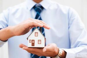 Hands holding a small house model, depicting safety and security in homeownership. photo