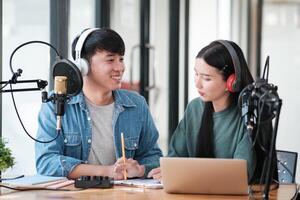 Two people are sitting at a desk with a laptop and a microphone photo