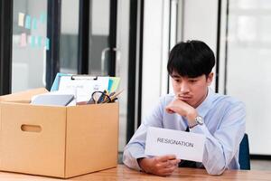 Man at desk with resignation letter, pondering his decision beside a packed box. photo