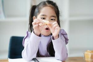 A young girl is sitting at a table with a piece of food in her hand photo