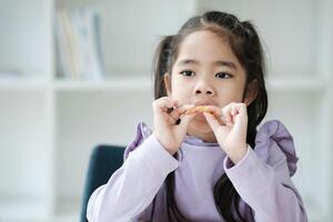 un joven niña es comiendo un bocadillo mientras sentado en un silla foto