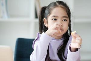 un joven niña es comiendo un bocadillo mientras sentado en un silla foto