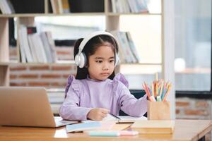 A young girl wearing headphones is sitting at a desk with a laptop photo