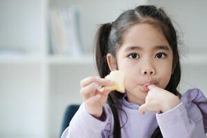 un joven niña es comiendo un pedazo de Fruta foto