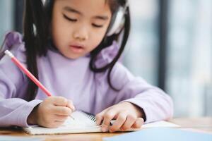 un joven niña es escritura en un cuaderno con un lápiz foto