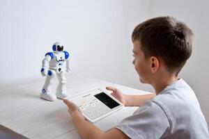 Boy is programming the work of a robot on a desk with a tablet in his hand photo