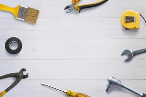 Top view of assorted tools neatly arranged on a white wooden desk, with copy space in the center. Flat lay composition ideal for DIY concept promotion photo