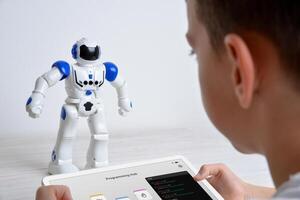 Boy controls robot using tablet on desk. Illustrating education, technology, innovation, and interactive learning experiences in robotics and programming photo