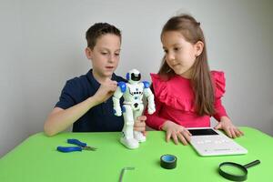 Girl and boy assemble large white object on workbench, programming its functions. Concept of teamwork, technology, learning and innovation photo