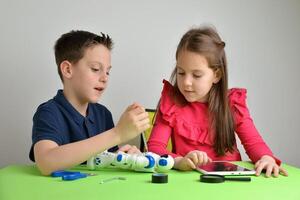 Children assemble robot on work table, engaging in conversation. Concept of teamwork, collaboration, education, and hands-on learning experience photo