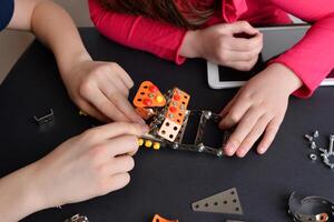 Children assemble robot, showcasing engineering skills. Top-down view of table. Concept of education, creativity, and hands-on learning photo