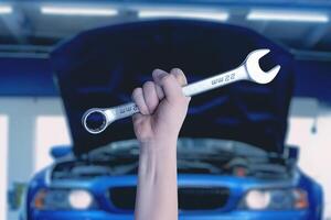 Wrench in hand in front of a blue car with an open engine compartment. Ready for service and maintenance. Professional automotive concept photo