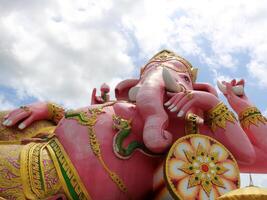 Close up view of bright pink or magenta painted Ganesha concrete statue recline posture with sunlight and white cloudy background, Thailand. photo