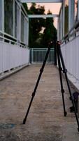 black camera tripod with iron guardrail posts in the background. photo