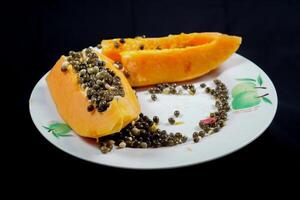 close up view of papaya fruit isolated on plate on black background. photo