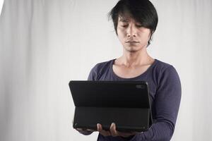 retrato de joven asiático hombre en pie y participación ordenador portátil computadora cuaderno en tecnología dispositivo aislado en blanco antecedentes. estilo de vida de negocio gente. foto