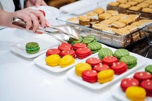 The distribution table in the cafe sweets lie on a plate, the hand takes cookies with tongs, colored macaroons, delicious pastries, cuisine in the restaurant. photo