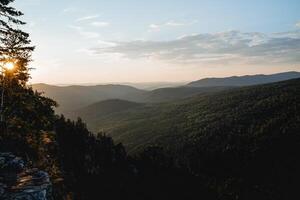 the landscape of the hilly mountains at sunset, the perspective of the horizon extending into the distance, the sun shining through the trees, the golden hour in photography. photo