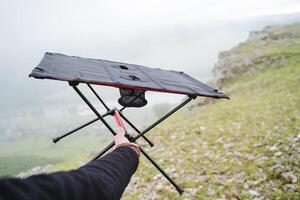 Compact folding table for camping in nature, camping equipment dining table, hand holds the frame of the table. photo