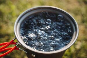 Bubbles of boiling water in a pot, warm water for tea, bubbling liquid, camp utensils for cooking, top view of the water. photo