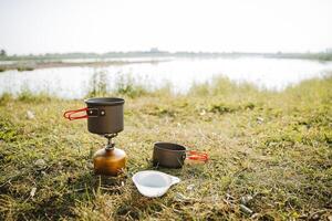 Camping in nature by the river, the concept of a tourist kitchen on a hike, a set of plates with handles, dishes for cooking on a gas burner on a hike. photo